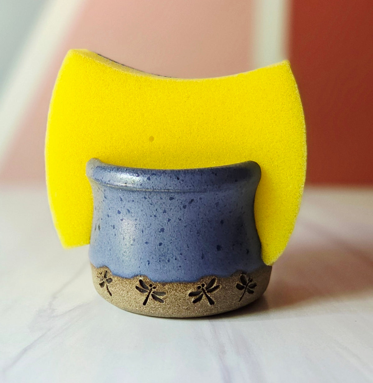 Purple stoneware sponge holder with dragonfly design holding a yellow sponge on a white background