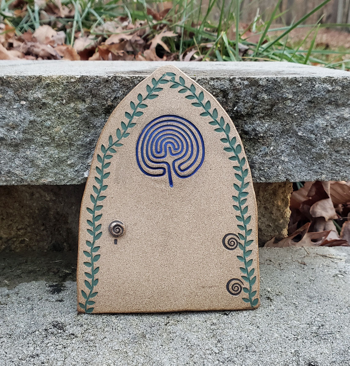 Stoneware fairy door with a blue labyrinth design on a stone surface