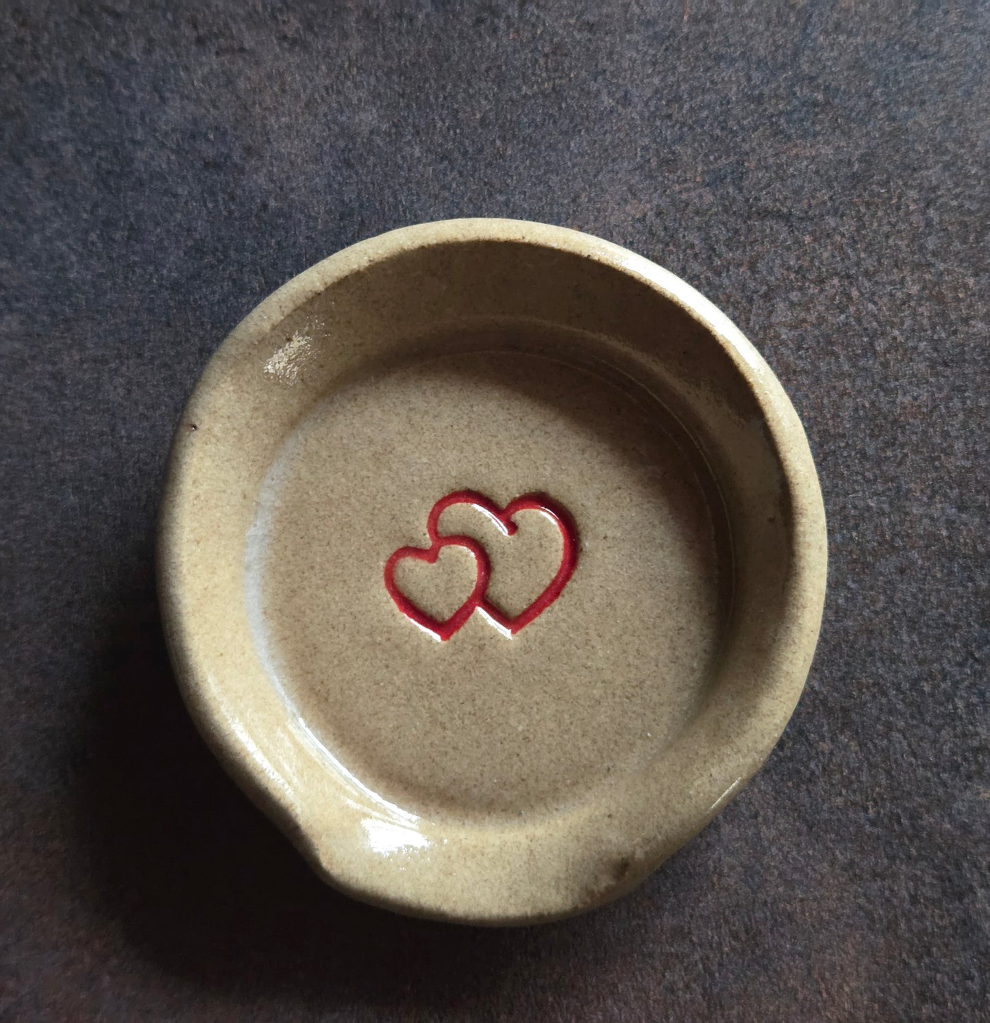 Stoneware teaspoon rest with double heart design on a dark surface