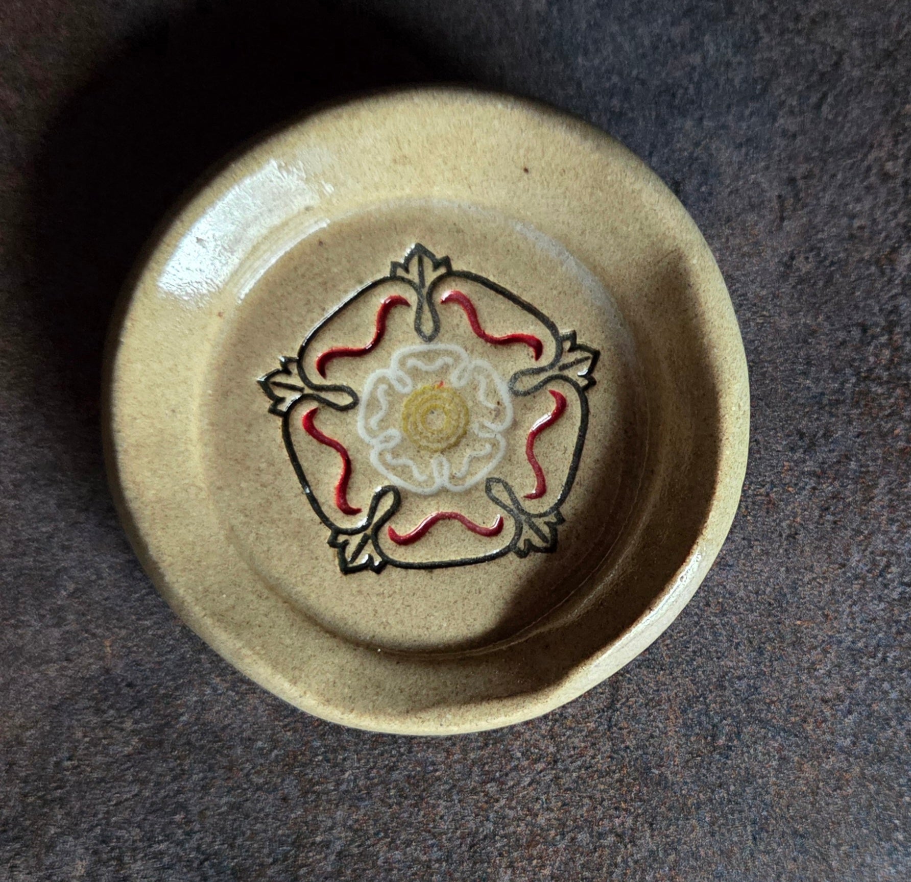 Stoneware teaspoon rest with Tudor rose design on a dark surface