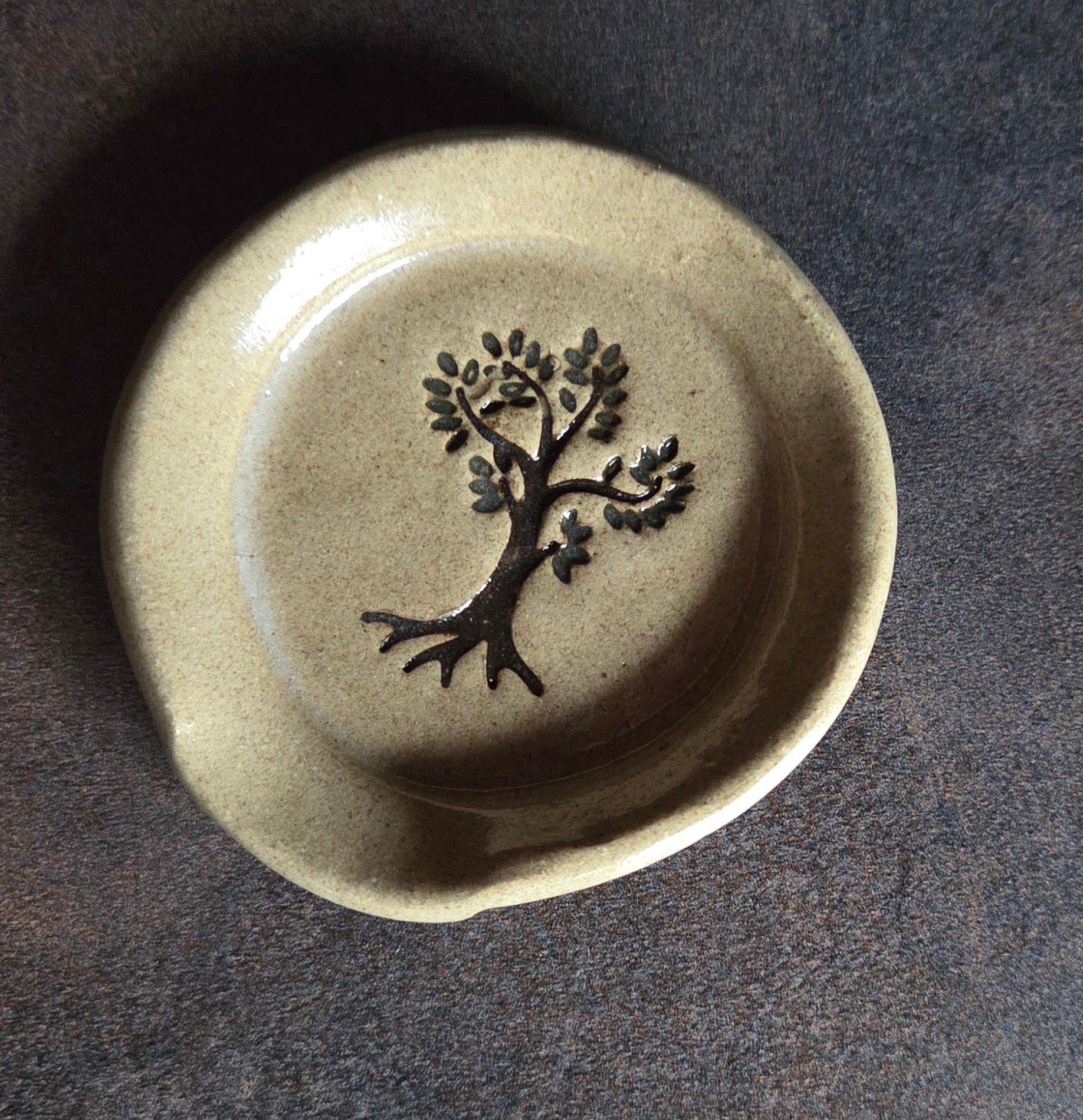 Stoneware teaspoon rest with tree of life design on a dark surface