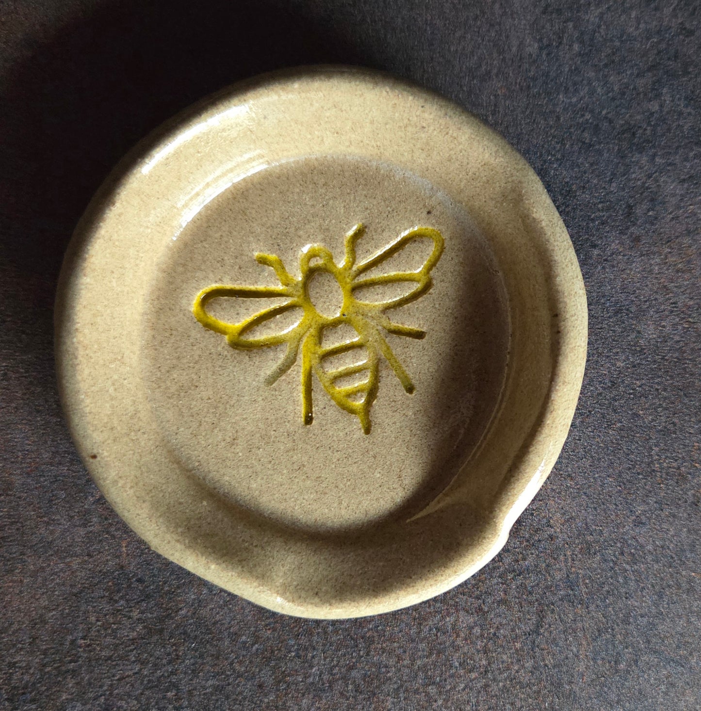 Stoneware teaspoon rest with bee design on a dark surface