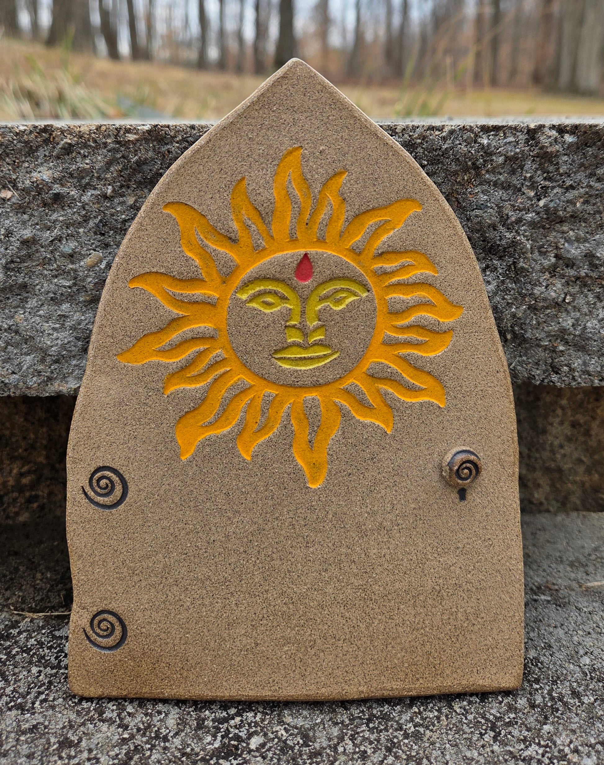 Stoneware fairy door with sun design on a concrete surface