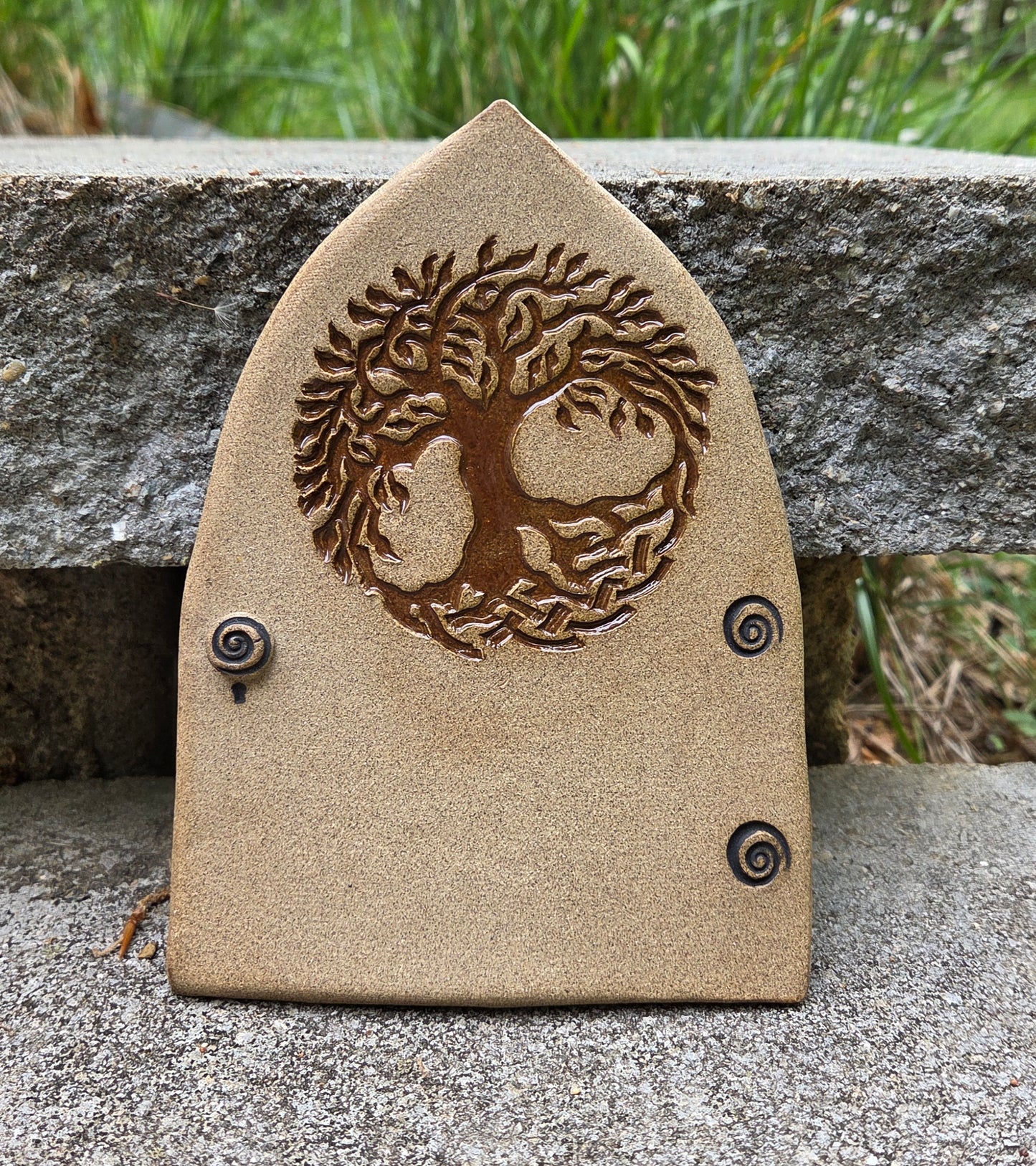 Stoneware fairy door with tree of life design on a concrete surface