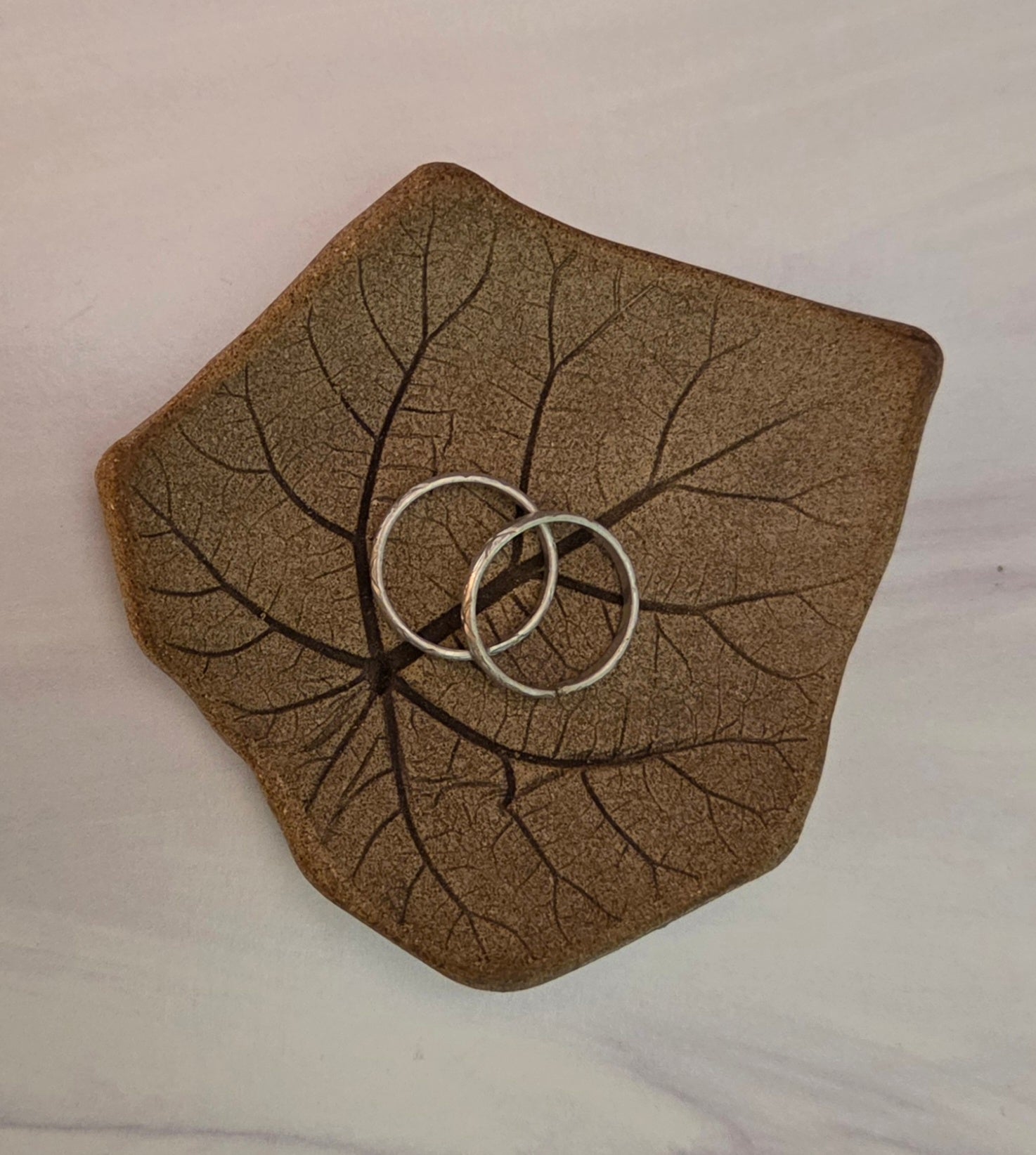 Two silver rings on a leaf-impressed stoneware dish