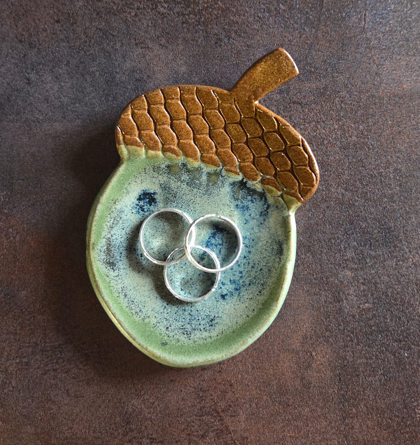Stoneware acorn-shaped trinket dish with rings on a brown background