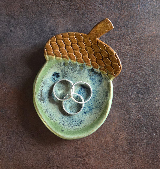 Stoneware acorn-shaped trinket dish with rings on a brown background