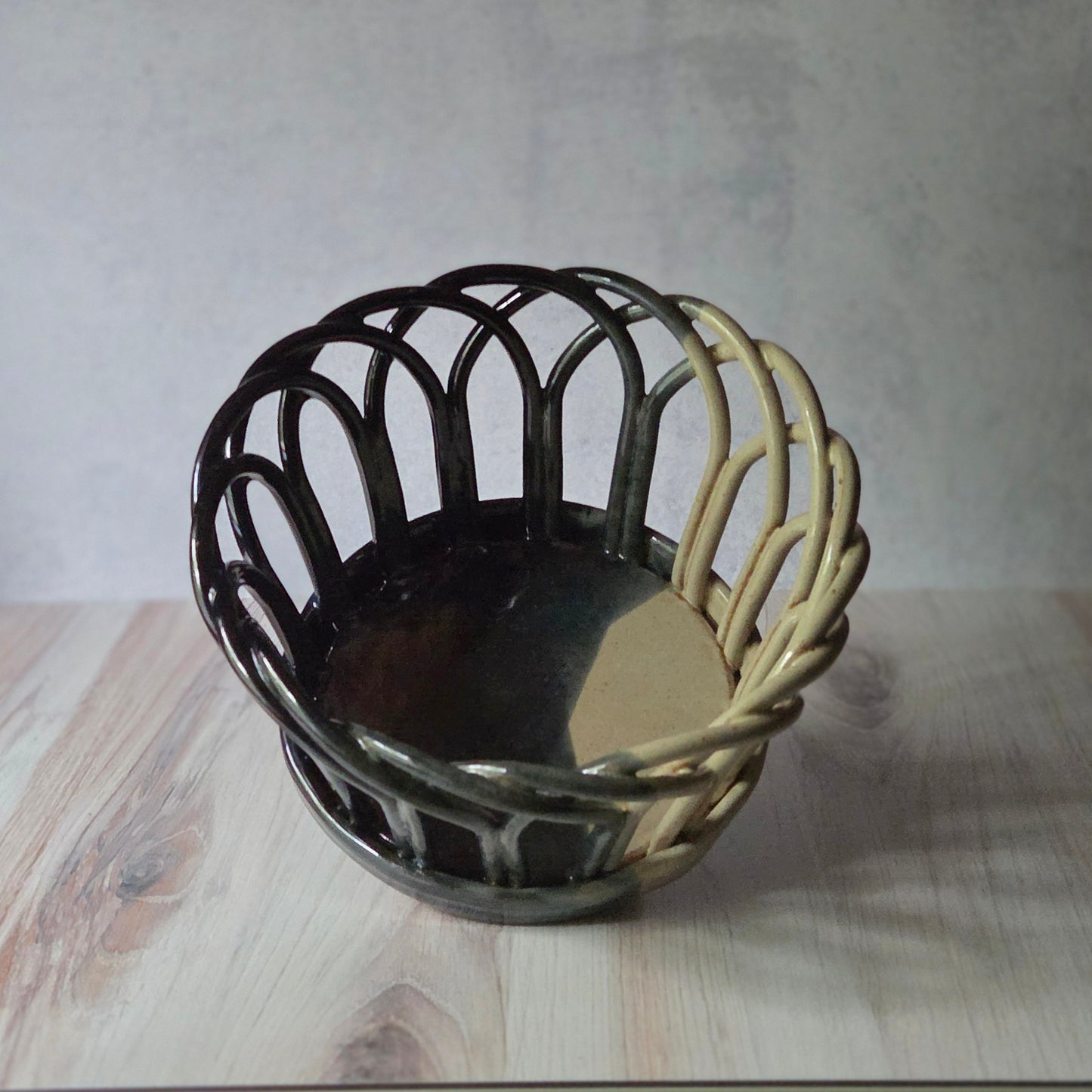 Black and eggshell stoneware basket, on a wooden surface with a neutral background.