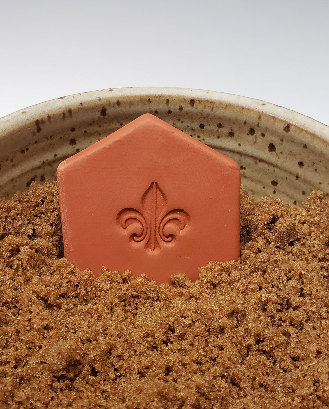 brown sugar keeper with Fleur-di-lis design in a bowl of brown sugar