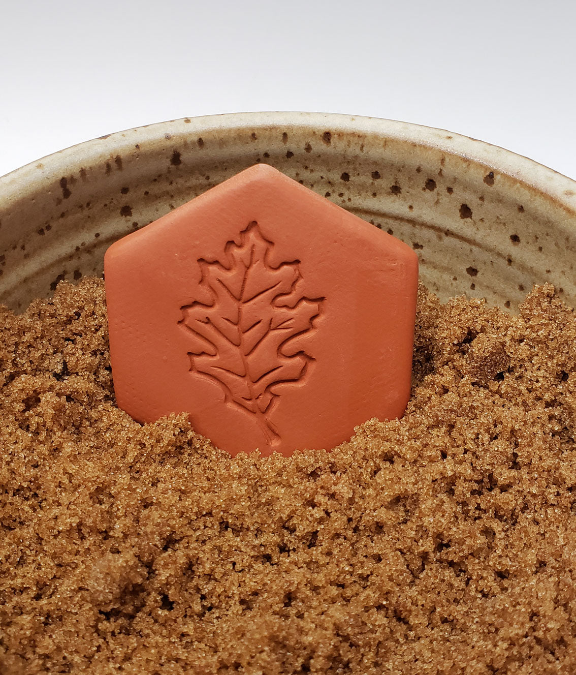 brown sugar keeper with oak leaf design in a bowl of brown sugar