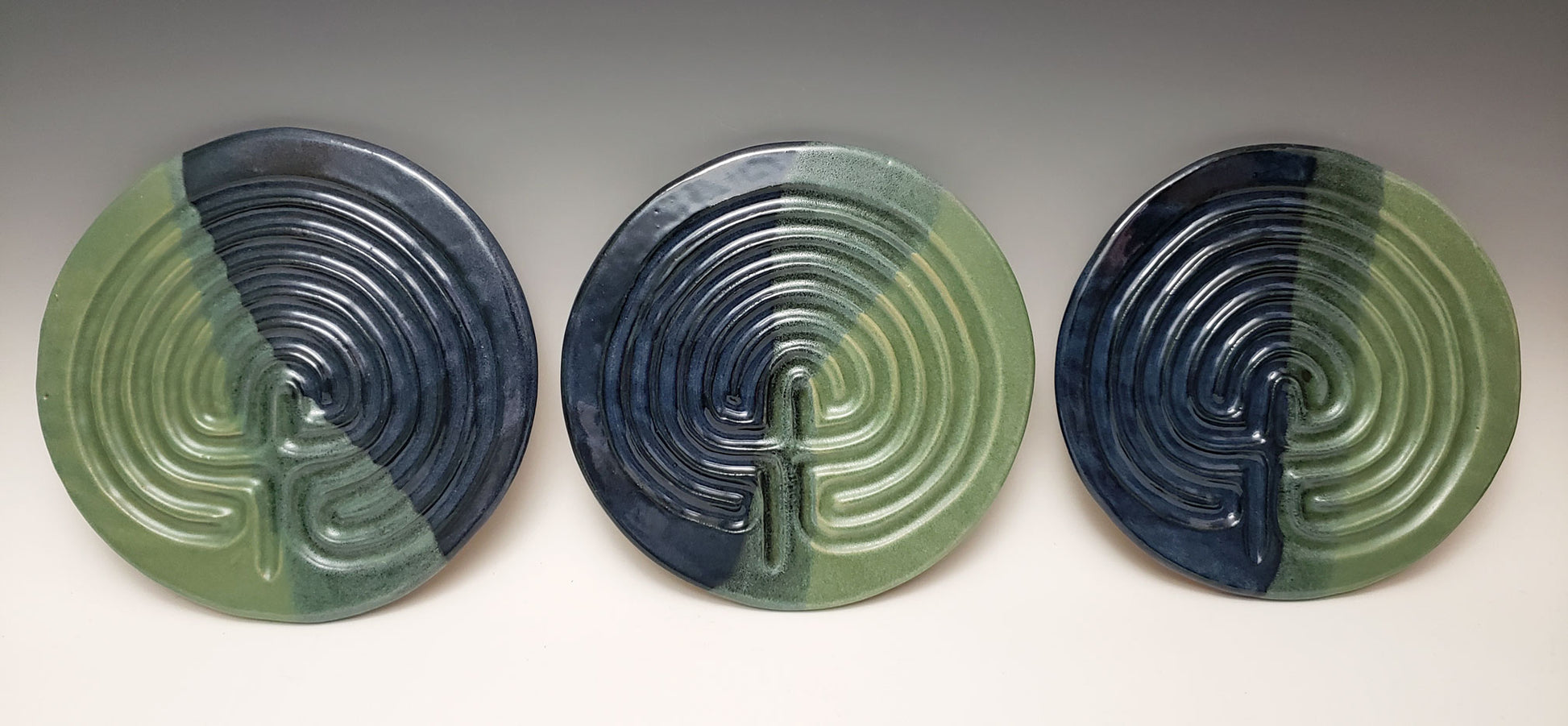 Three stoneware finger labyrinths in green and dark blue on a white background