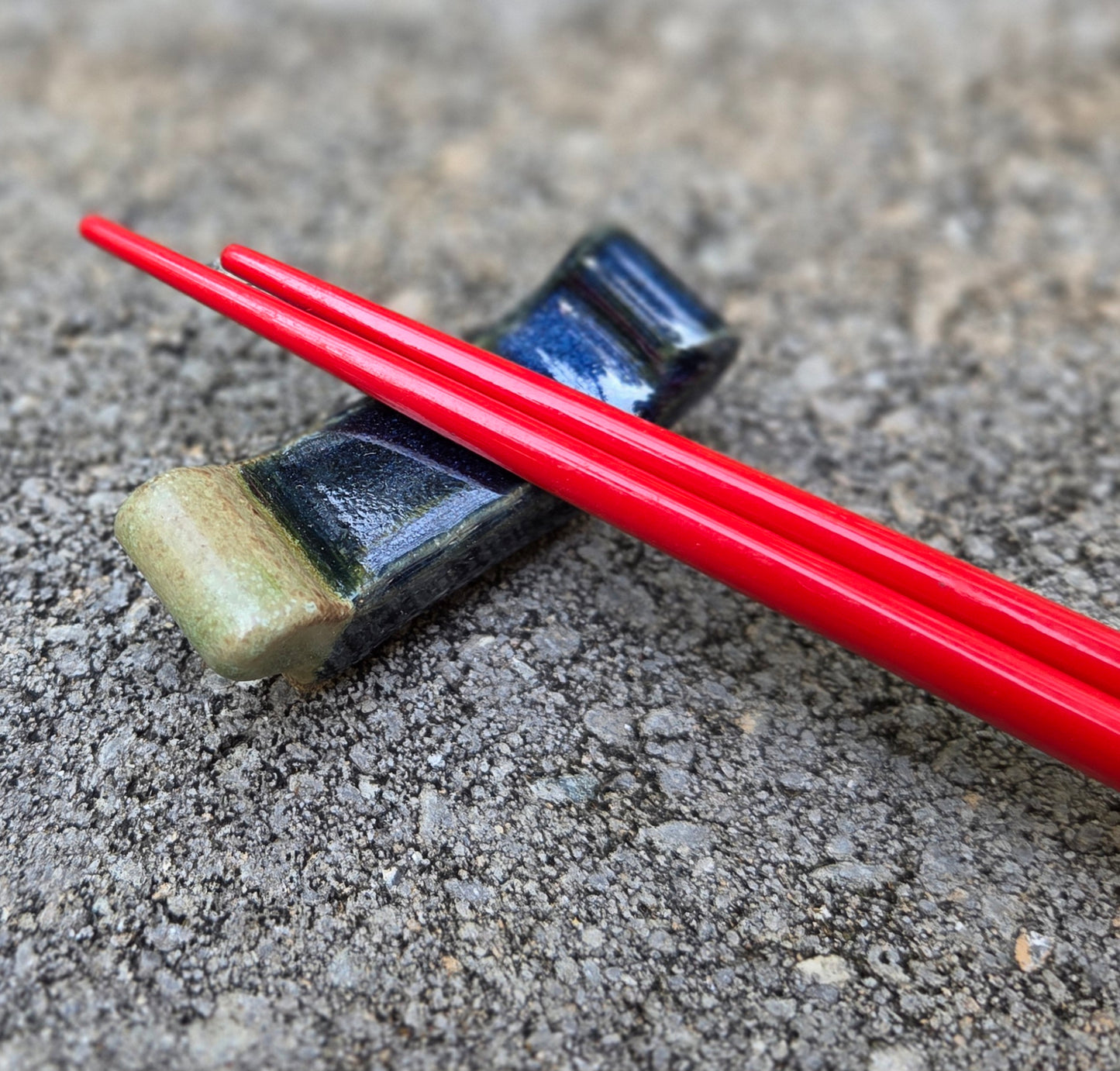 Stoneware chopstick rests with dark blue and moss glaze design with red chopsticks sitting on a stone surface