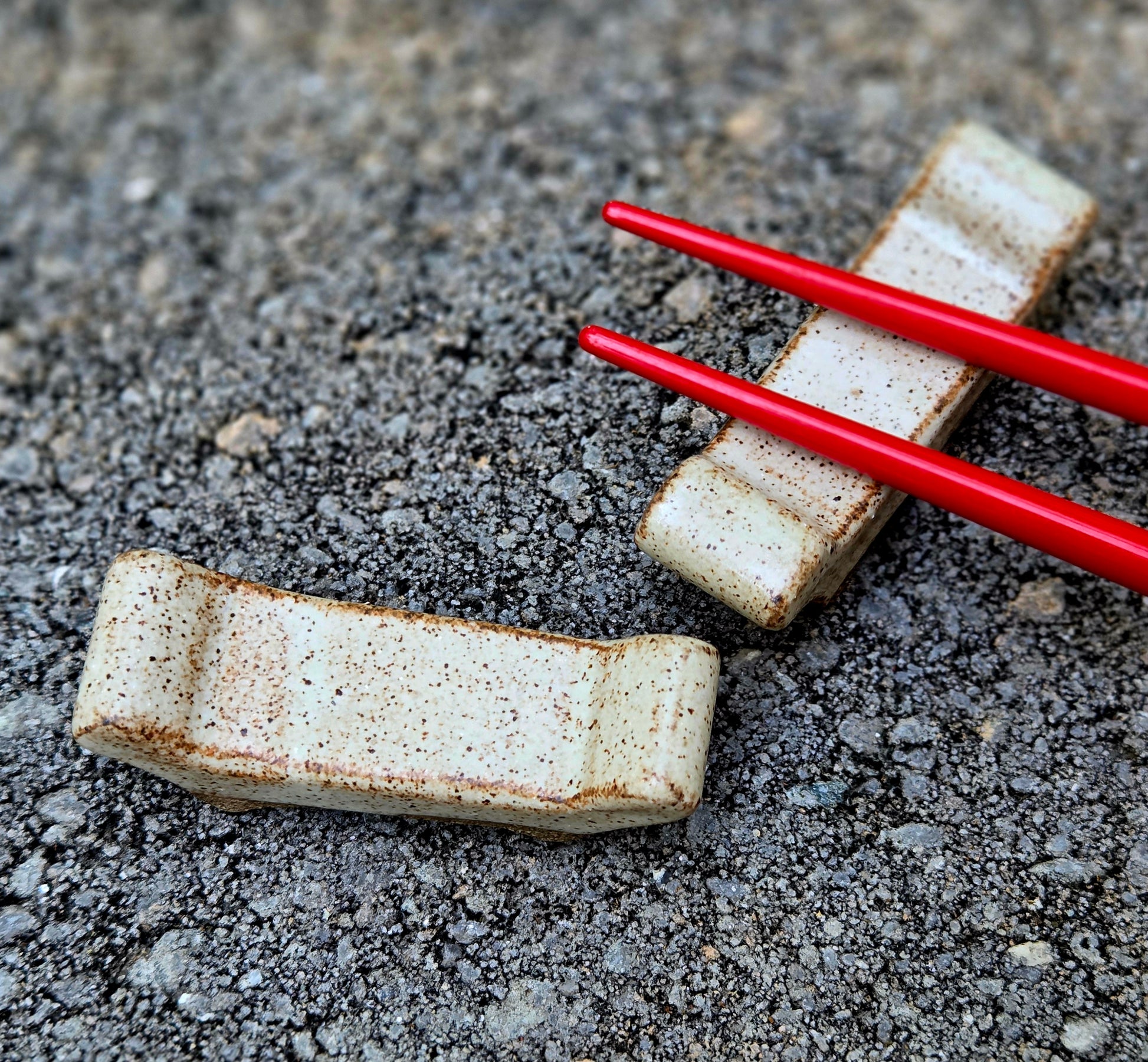 Two stoneware chopstick rests with eggshell glaze with red chopsticks sitting on a stone surface