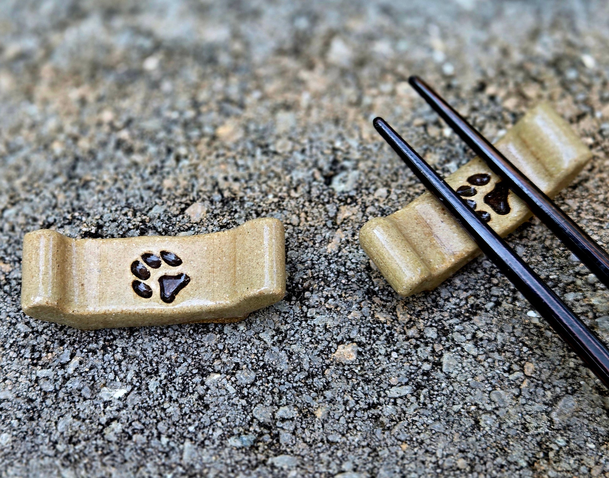 Two stoneware chopstick rests with a paw print design with black chopsticks sitting on a stone surface