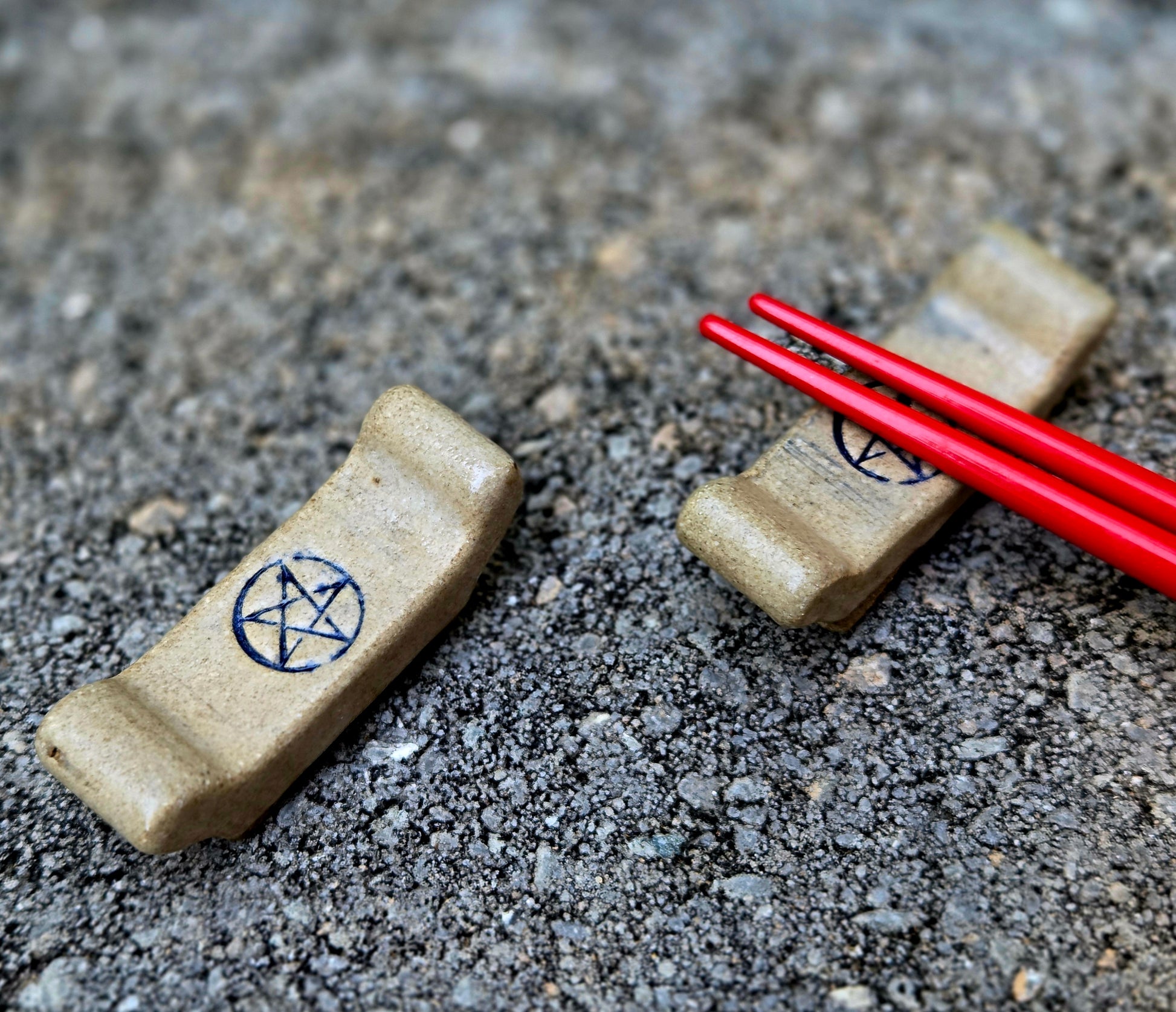 Two stoneware chopstick rests with a pentagram design with red chopsticks sitting on a stone surface