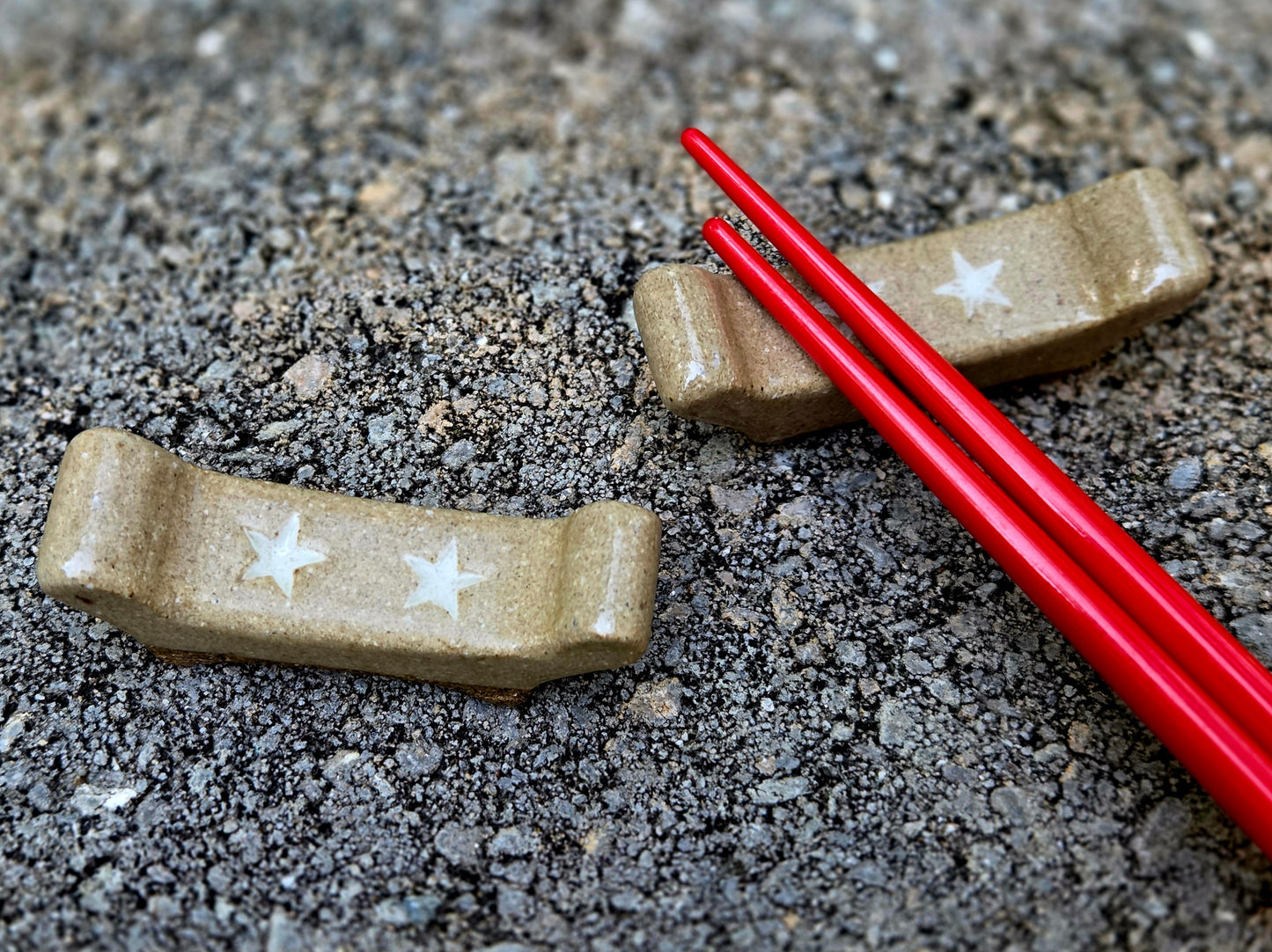 Two stoneware chopstick rests with a double star design with red chopsticks sitting on a stone surface