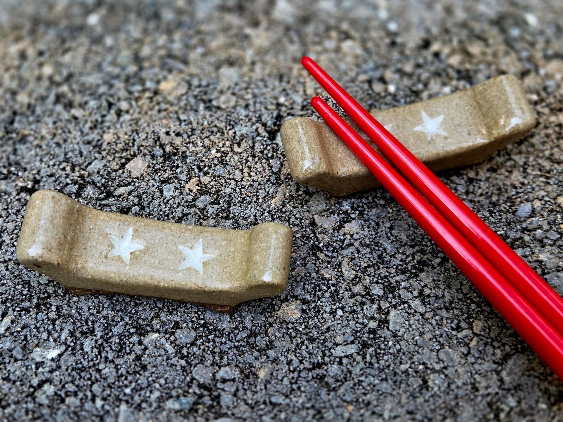 Two stoneware chopstick rests with a double star design with red chopsticks sitting on a stone surface