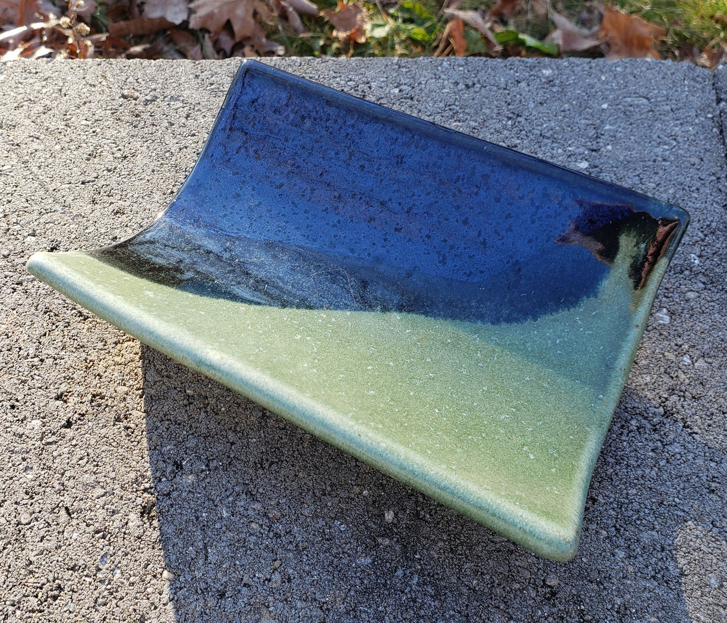 Stoneware crescent tray with blue & green glaze on a concrete surface