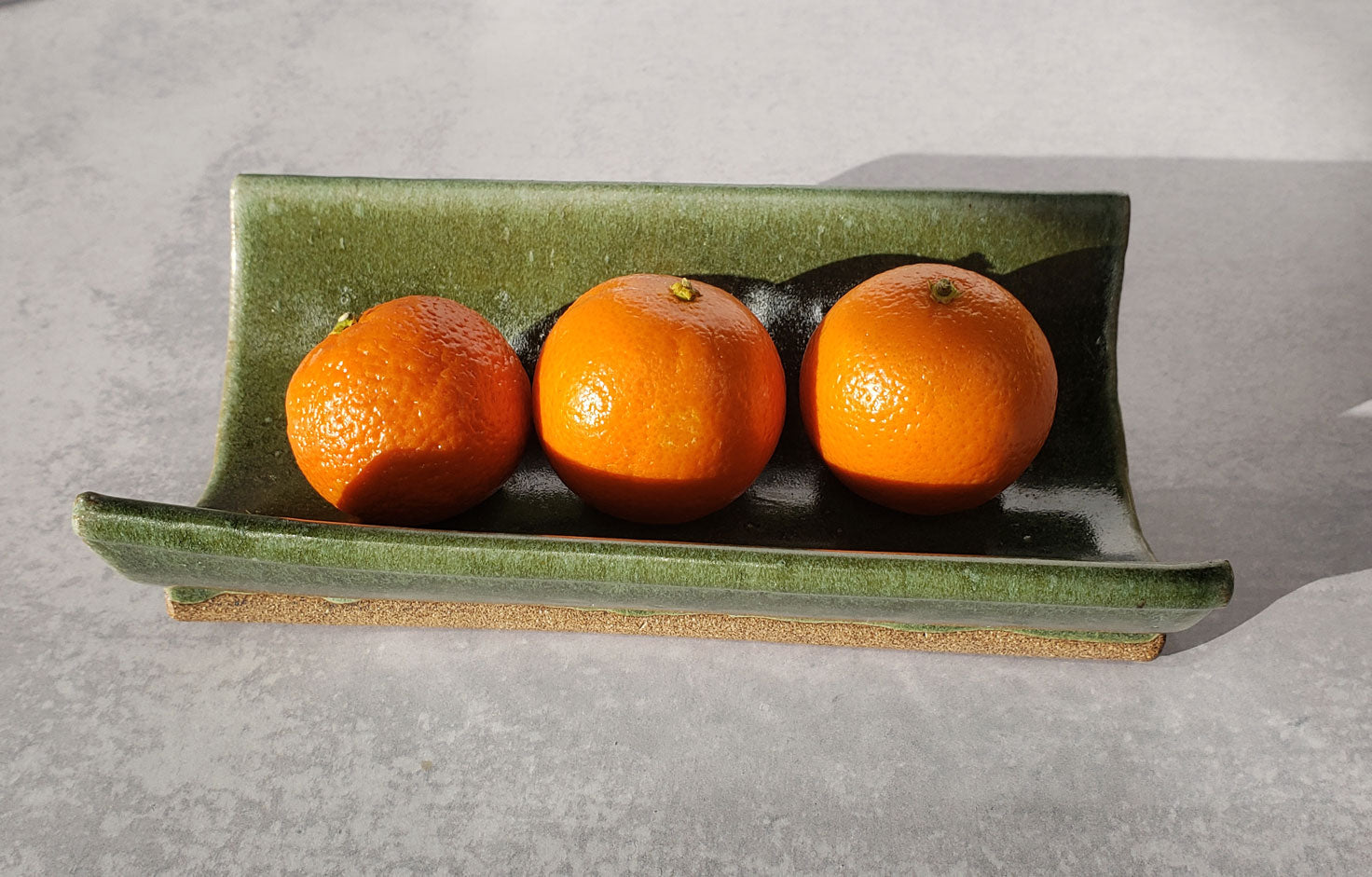 Three small oranges on a green crescent tray with a gray background