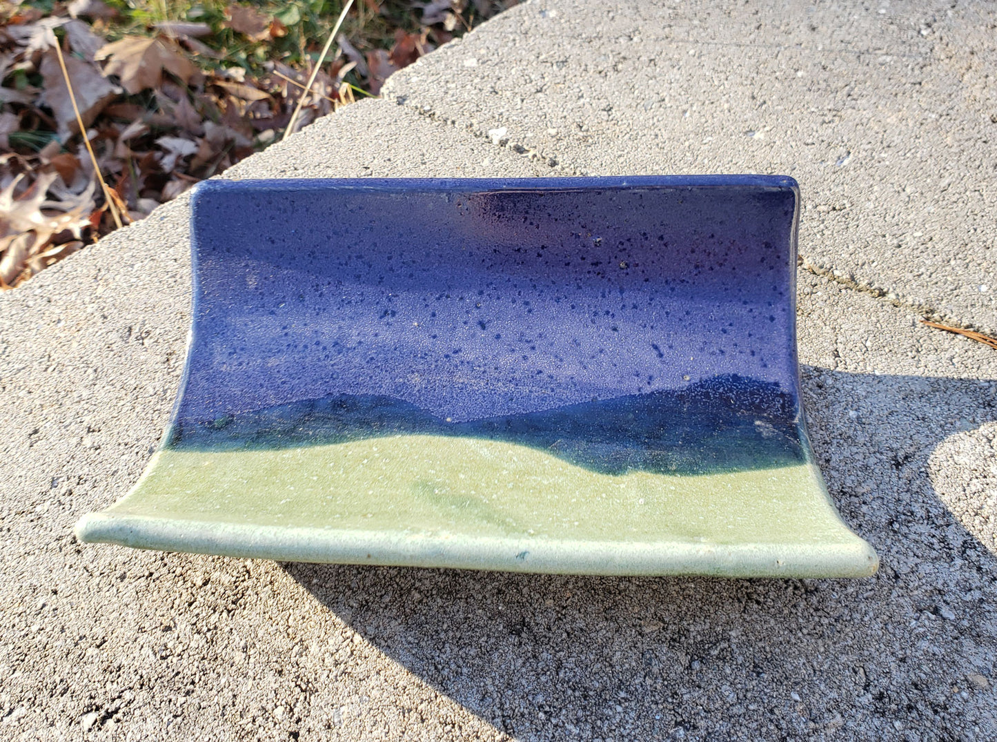 Ceramic crescent tray with purple & green glaze on a concrete surface