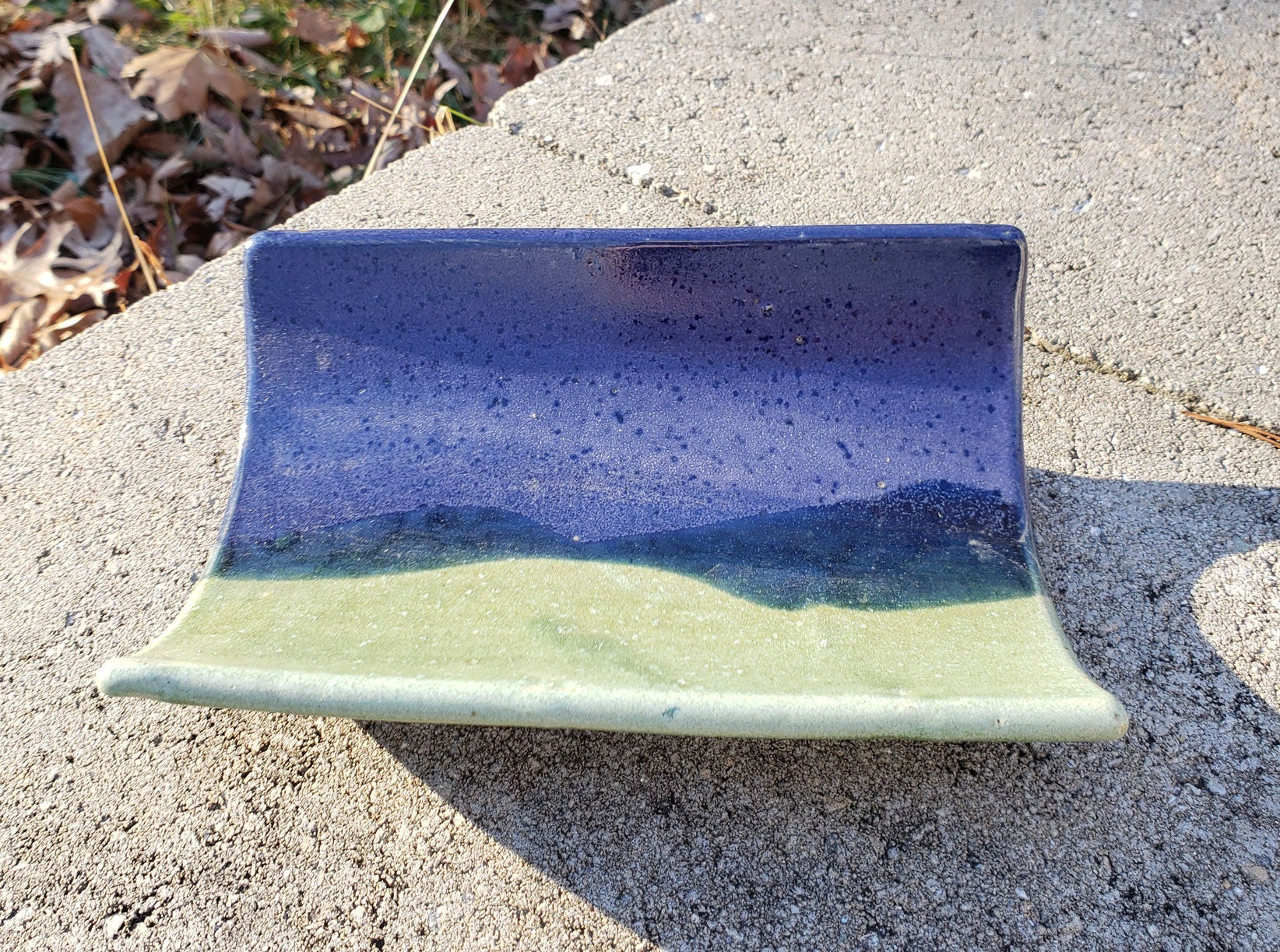 Ceramic crescent tray with purple & green glaze on a concrete surface