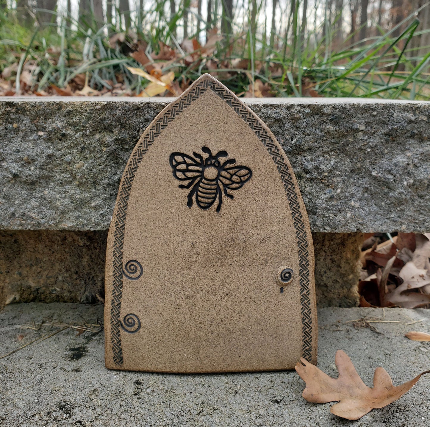 Stoneware fairy door with bee design on a stone surface outdoors