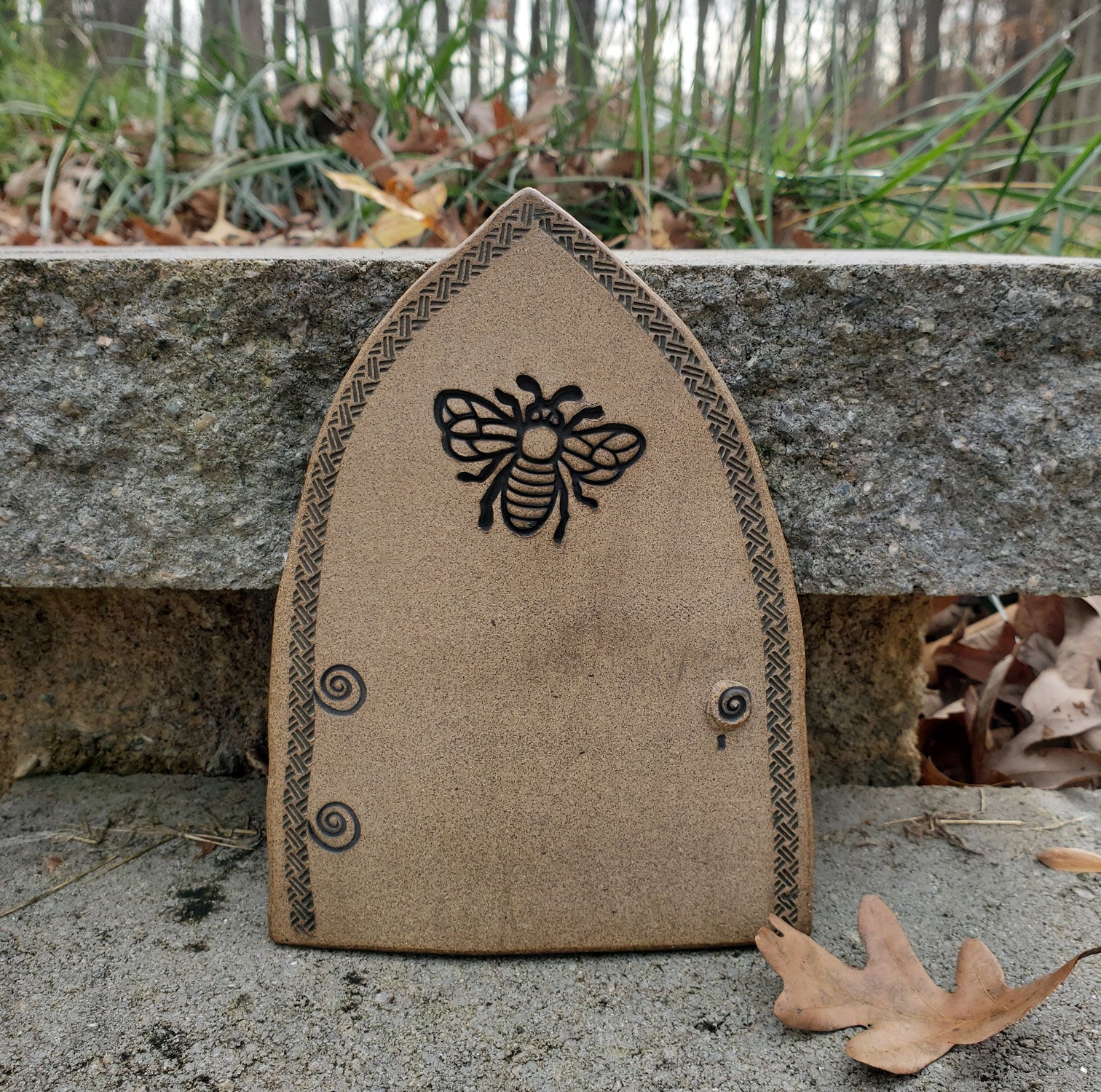 Stoneware fairy door with bee design on a stone surface outdoors