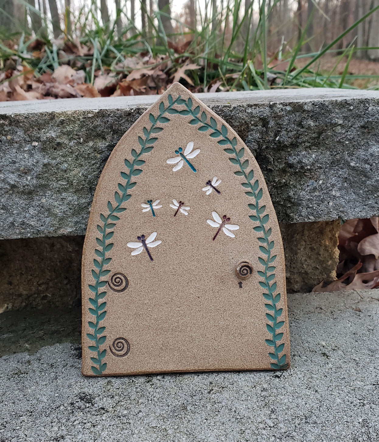 Stoneware fairy door with dragonfly  design on a stone surface outdoors