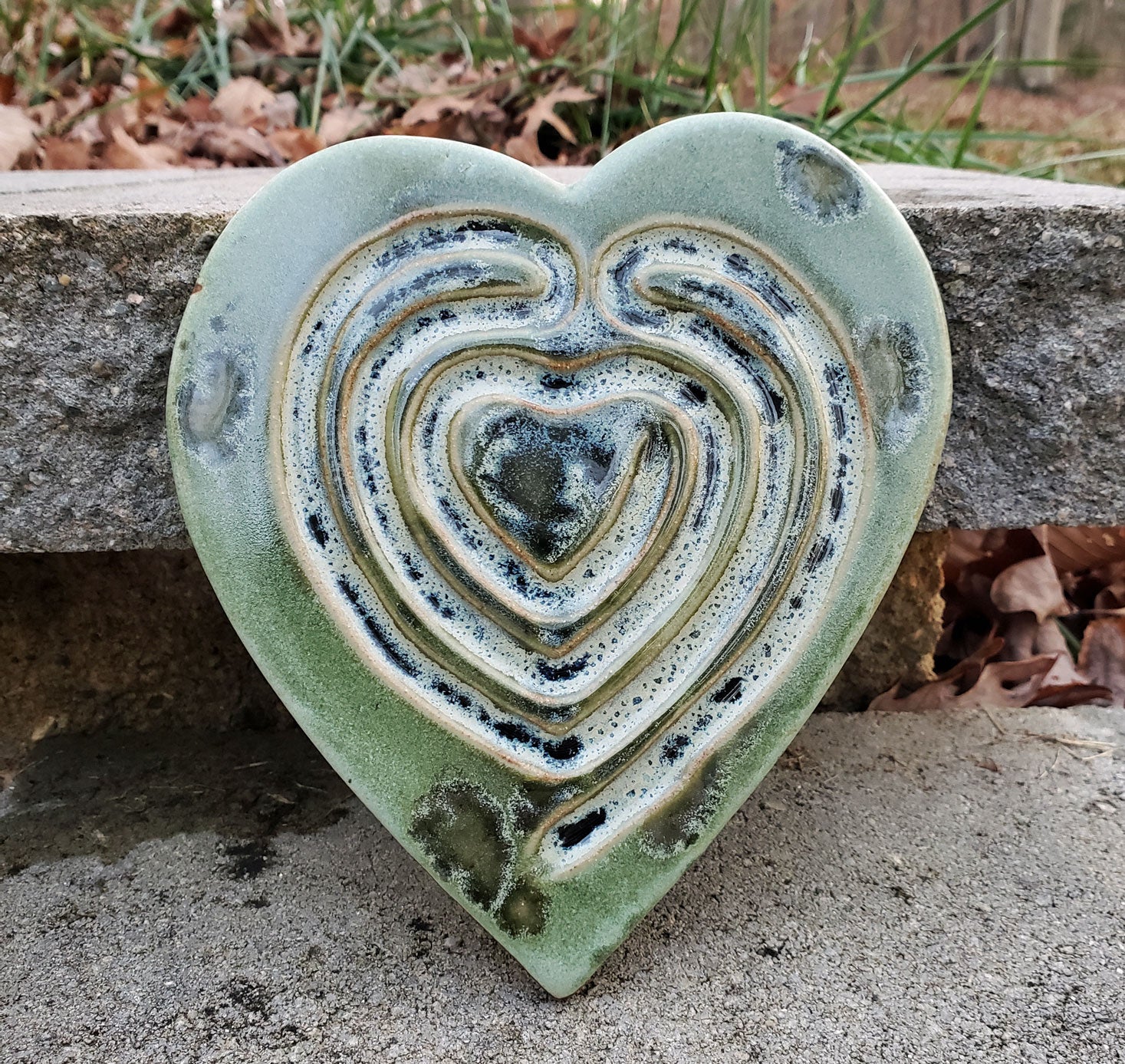 Heart-shaped, green ceramic labyrinth on a stone surface.