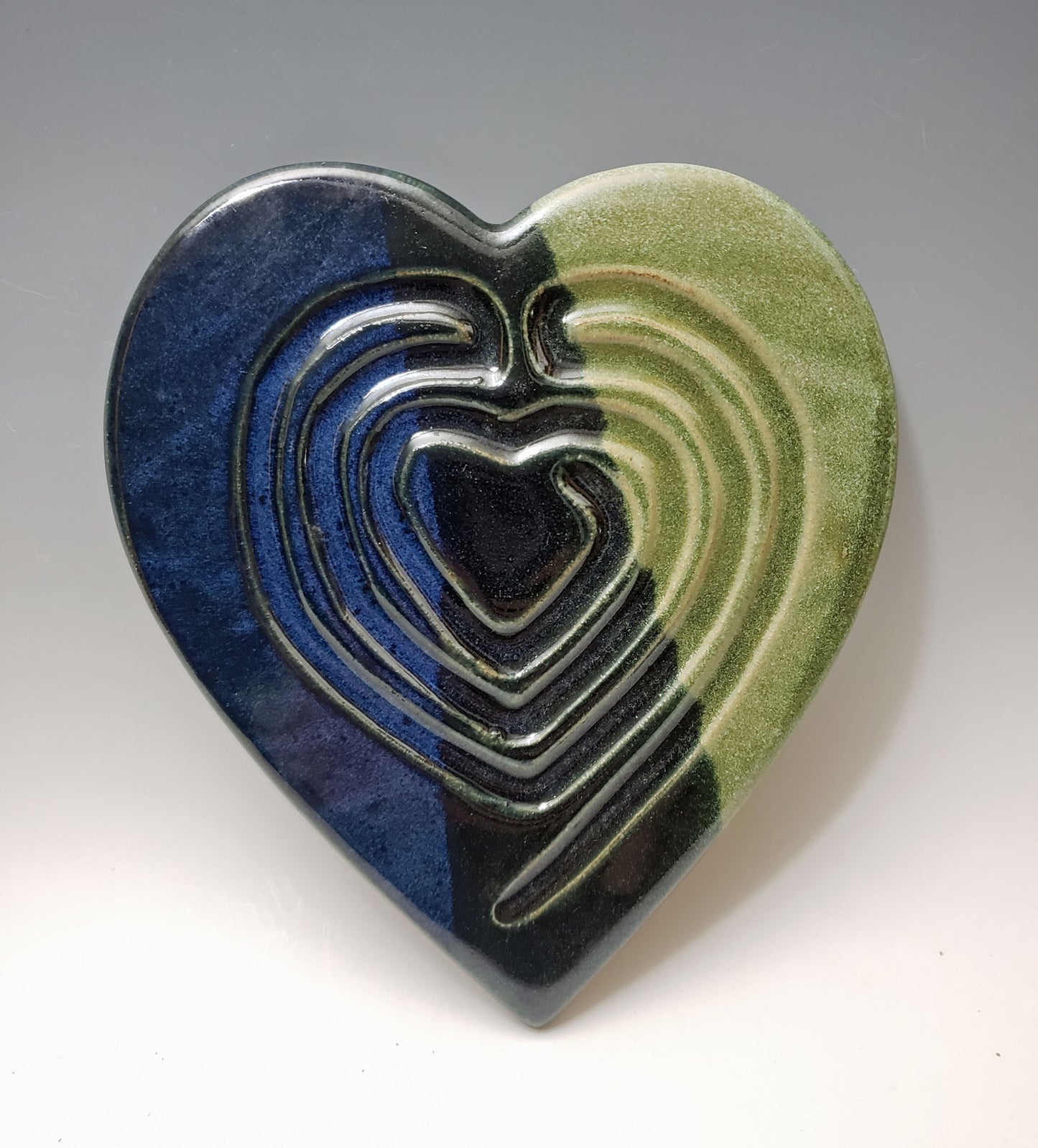 Heart-shaped ceramic labyrinth with blue and green glazes on a gray background