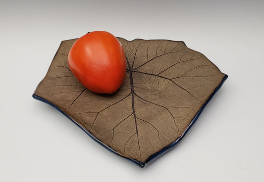 Persimmon on a large leaf stoneware plate with a white background