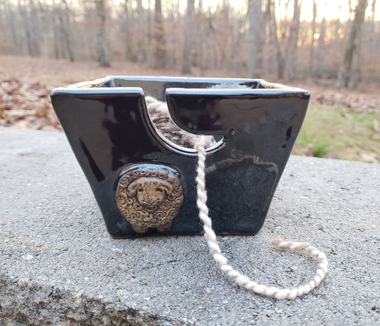 Black stoneware yarn bowl with decorative sheep on a concrete surface with a forest background