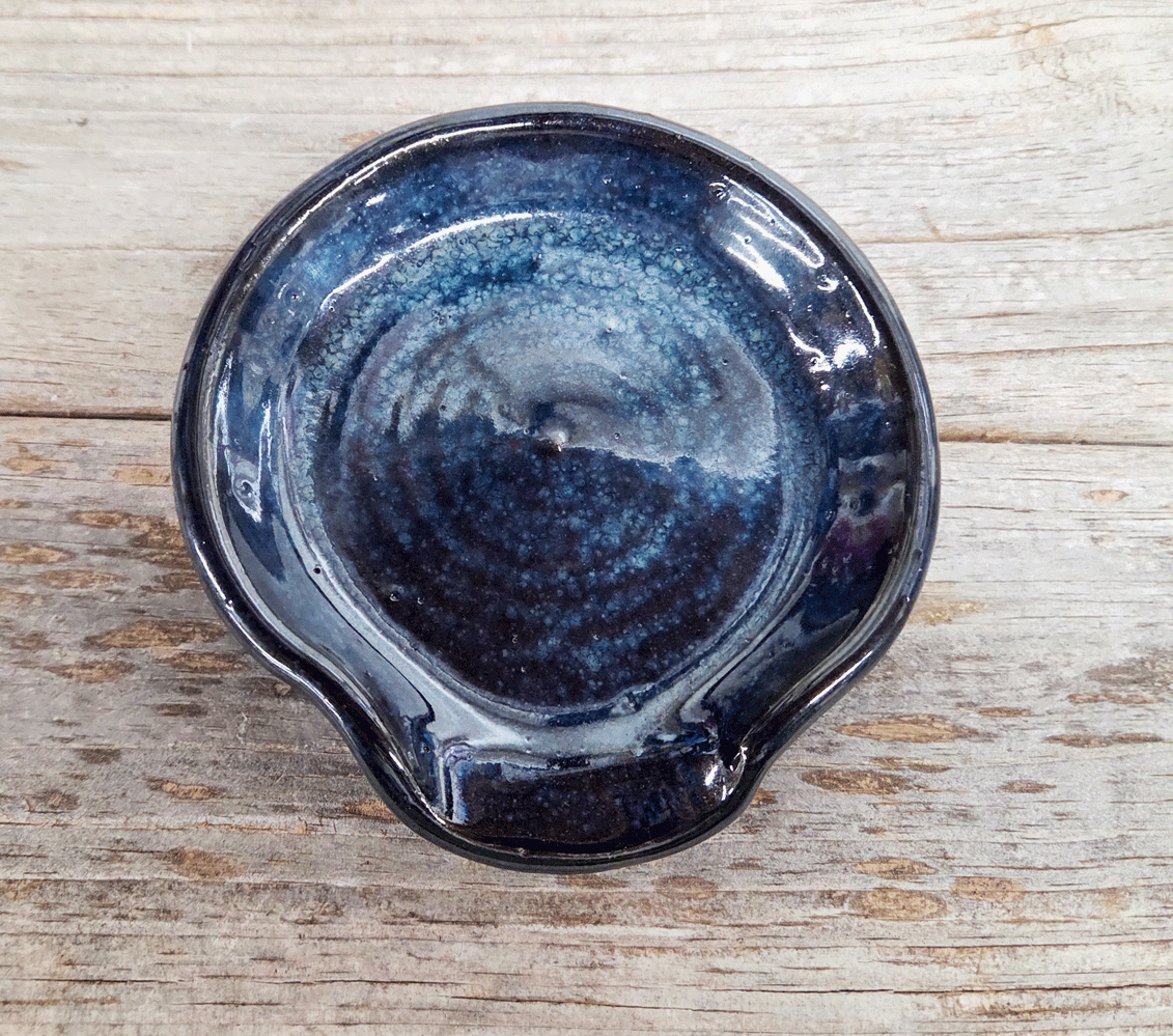 Stoneware spoon rest in black cosmos glaze on a wooden surface