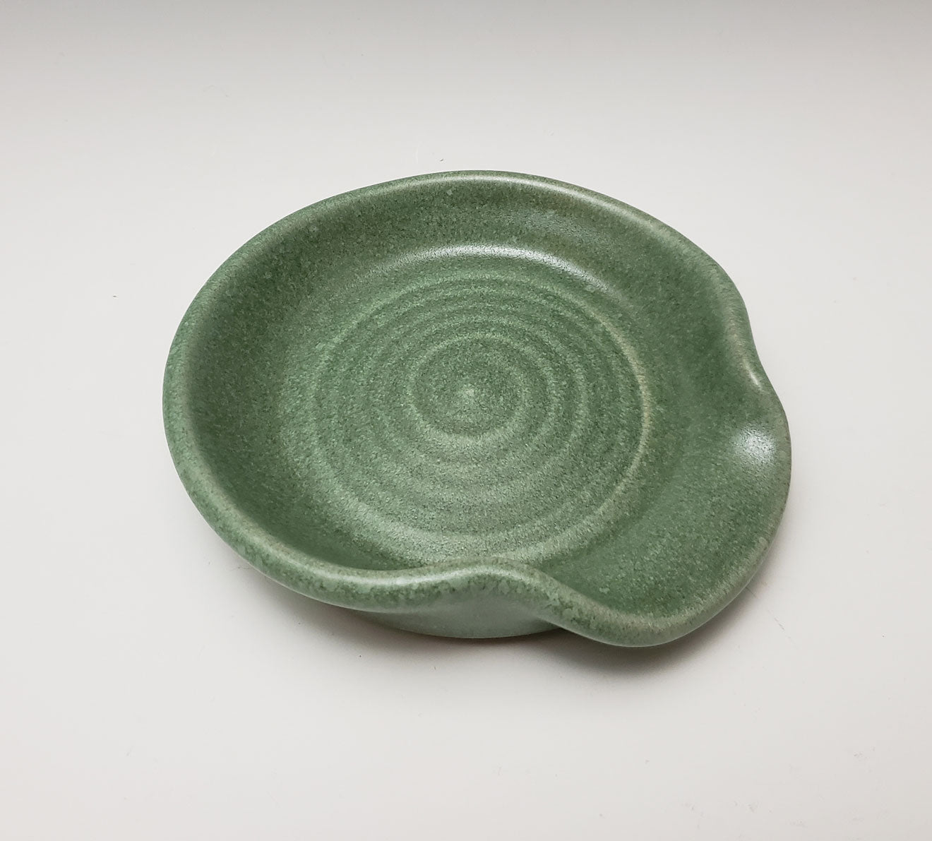 Green ceramic spoon rest with a spiral design on a white background