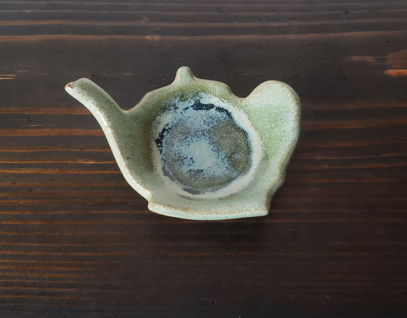 Ceramic teapot-shaped tea bag caddy on a wooden surface